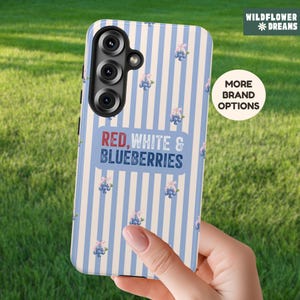 May include: A smartphone case with a blue and white striped pattern, adorned with small floral and blueberry illustrations. The case features the text "RED, WHITE & BLUEBERRIES" and the brand name "WILDFLOWER DREAMS".