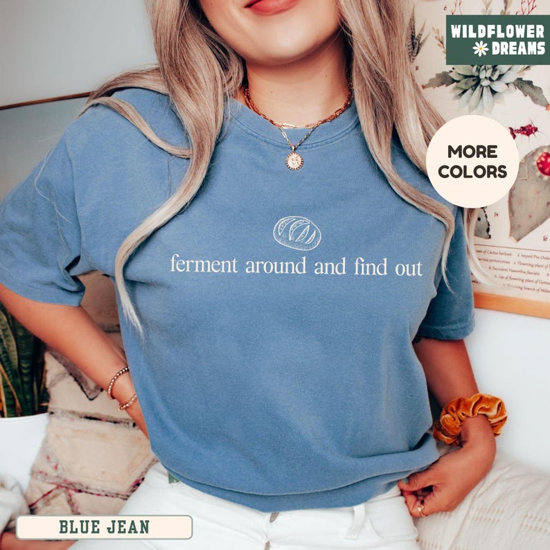 May include: Blue jean colored t-shirt with the text "ferment around and find out" in white. The shirt features a white graphic of a loaf of bread above the text. The shirt is a crew neck style.