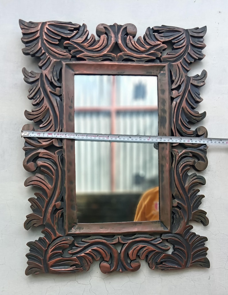 May include: Ornate rectangular mirror with a dark brown, carved wooden frame. The frame features detailed, swirling leaf and scroll designs. The mirror's dimensions are approximately 20 inches wide.
