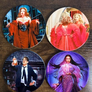 Könnte beinhalten: Set aus vier runden Untersetzern mit Bildern von Filmfiguren. Die Untersetzer zeigen lebendige Bilder von Frauen in roten und lila Kleidern und einem Mann, der eine Flasche hält. Die Untersetzer sind für Getränke bestimmt.