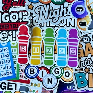 May include: A collection of bingo-themed stickers featuring colourful bingo daubers in red, yellow, green, blue, and purple, each labelled with letters B, I, N, G, O. The background includes bingo cards, numbered balls, and text like Bingo Night.