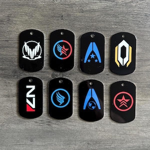 Puede incluir: Ocho placas de identificación negras con varios diseños gráficos blancos, azules, rojos y amarillos. Cada placa tiene un pequeño agujero en la parte superior. Los diseños incluyen símbolos estilizados y las letras "N7".