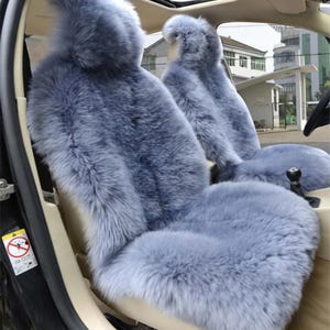 Könnte beinhalten: Hellblaue Autositzbezüge aus Kunstfell. Die Bezüge sind für die Vordersitze eines Fahrzeugs konzipiert. Das flauschige Material hat eine einfarbige hellblaue Farbe und sorgt für ein weiches und komfortables Aussehen. Der Innenraum des Autos ist im Hintergrund sichtbar.