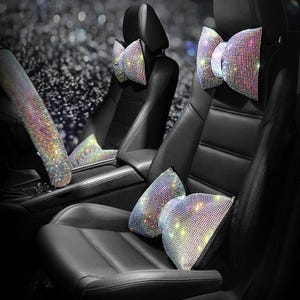 Könnte beinhalten: Schwarze Autositze mit dekorativem Strass-Zubehör. Das Bild zeigt eine Lenkradabdeckung, Kopfstützenkissen und Sitzkissen, die alle mit glitzernden Strasssteinen bedeckt sind. Das Zubehör verleiht dem Innenraum des Autos einen Hauch von Glamour.