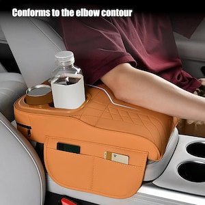 May include: Orange car seat organizer with cup holders, a bottle holder, and pockets for cards and a phone. The text "Conforms to the elbow contour" is visible. The organizer is designed to fit the car's center console.