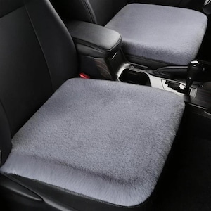 Puede incluir: Fundas de asiento de coche de felpa gris. Las fundas son rectangulares y se ajustan a los asientos del coche. Las fundas están hechas de un material suave y difuso. Los asientos del coche son negros.