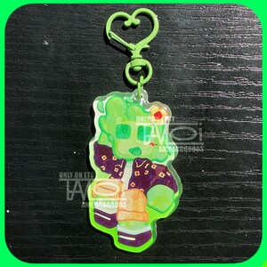 K&ouml;nnte beinhalten: Ein gr&uuml;ner Acryl-Schl&uuml;sselanh&auml;nger mit einer Cartoon-Figur mit gr&uuml;nem Teint, die eine lila Jacke mit Blumendetails tr&auml;gt. Der Schl&uuml;sselanh&auml;nger hat einen herzf&ouml;rmigen Verschluss und enth&auml;lt den Text "ONLY ON ETS" und "ANTACOGOODS".