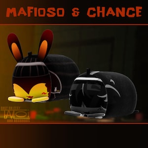 Pode incluir: Brinquedos de pel&uacute;cia com um design de coelho de desenho animado. Um brinquedo &eacute; preto e marrom com orelhas laranja e detalhes amarelos. O outro brinquedo &eacute; preto e branco. O texto "MAFIOSO & CHANCE" est&aacute; no topo.