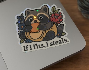 May include: A sticker featuring a cartoon raccoon holding a piece of toast. The raccoon is wearing a yellow shirt and surrounded by flowers. The text "If I fits, I steals" is below the raccoon.