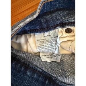 Pu&ograve; includere: Primo piano dell'interno di jeans blu. Un'etichetta bianca &egrave; visibile con testo tra cui "MADE IN BANGLADESH" e informazioni sulla taglia "34X32". I jeans sono realizzati in cotone e poliestere.