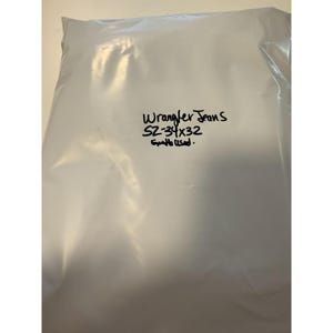 Pu&ograve; includere: Un sacchetto di plastica bianco con le parole "Wrangler Jeans" e la taglia "SZ-34x32" scritte con un pennarello nero. Il testo "Gentle Used" &egrave; anch'esso scritto sul sacchetto.