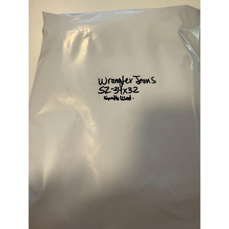 Pu&ograve; includere: Un sacchetto di plastica bianco con le parole "Wrangler Jeans" e la taglia "SZ-34x32" scritte con un pennarello nero. Il testo "Gentle Used" &egrave; anch'esso scritto sul sacchetto.
