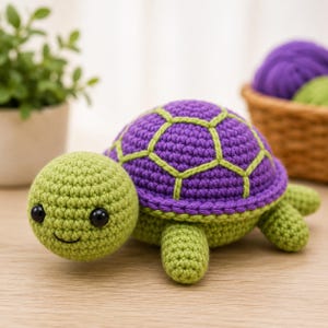 Könnte beinhalten: Ein gehäkeltes Schildkrötenspielzeug mit hellgrünem Kopf und Gliedmaßen sowie einem violetten Panzer, der mit hellgrünen Nähten akzentuiert ist. Die Schildkröte hat zwei kleine schwarze Kunststoffaugen und einen gestickten schwarzen Mund.
