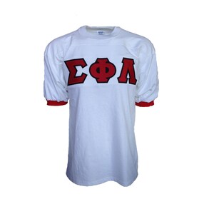 May include: White t-shirt with red and black "ΣΦΛ" lettering.