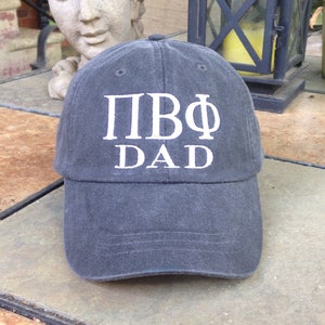 May include: A dark gray baseball cap with white embroidered text that reads "ПВФ DAD".