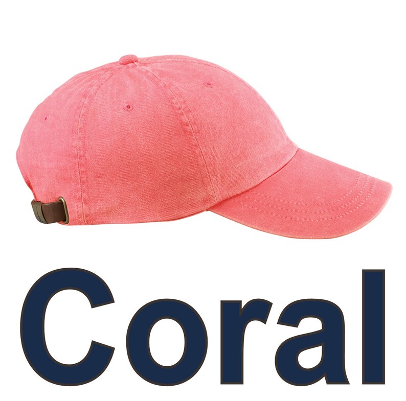 May include: Coral-colored baseball cap with a curved brim and adjustable strap. The cap is made of a soft, washed fabric. The word "Coral" is displayed in navy blue block letters below the cap.