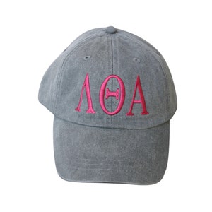 May include: A gray baseball cap with a pink embroidered Greek letter design that reads "ΛΘΑ".