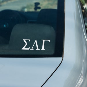 May include: A close-up of a silver car with a white "ΣΛΓ" sticker on the back window.