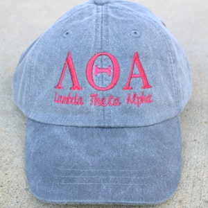 May include: A gray baseball cap with red embroidered letters that spell out "ΛΘΑ" and the words "Lambda Theta Alpha" below.