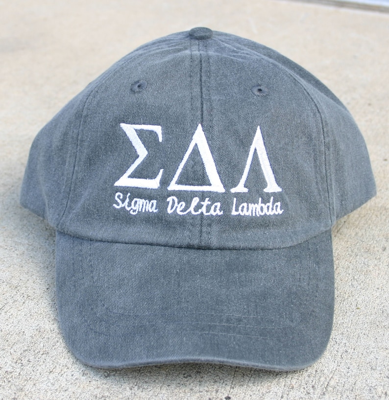 May include: A dark gray baseball cap with white embroidered letters that read "&Sigma;&Delta;&Lambda; Sigma Delta Lambda".
