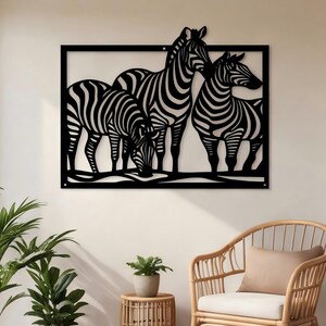 May include: A rectangular black metal wall art piece featuring a cutout design of three zebras standing together. The zebras are depicted with their characteristic striped patterns, enclosed within a simple black frame with visible mounting holes.