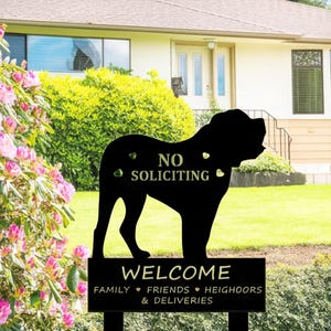 Op de afbeelding: Een zwart metalen tuinbord in de vorm van een hondensilhouet met de tekst NO SOLICITING. Daaronder toont een rechthoekige basis de tekst WELCOME FAMILY FRIENDS HEIGHOORS & DELIVERIES in witte letters met kleine hartjes.