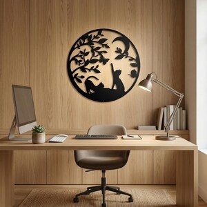 May include: Black metal wall art featuring a circular design with cat silhouettes under a tree, a crescent moon, and butterflies. The artwork is mounted on a wooden wall, creating a decorative piece for home or office decor.