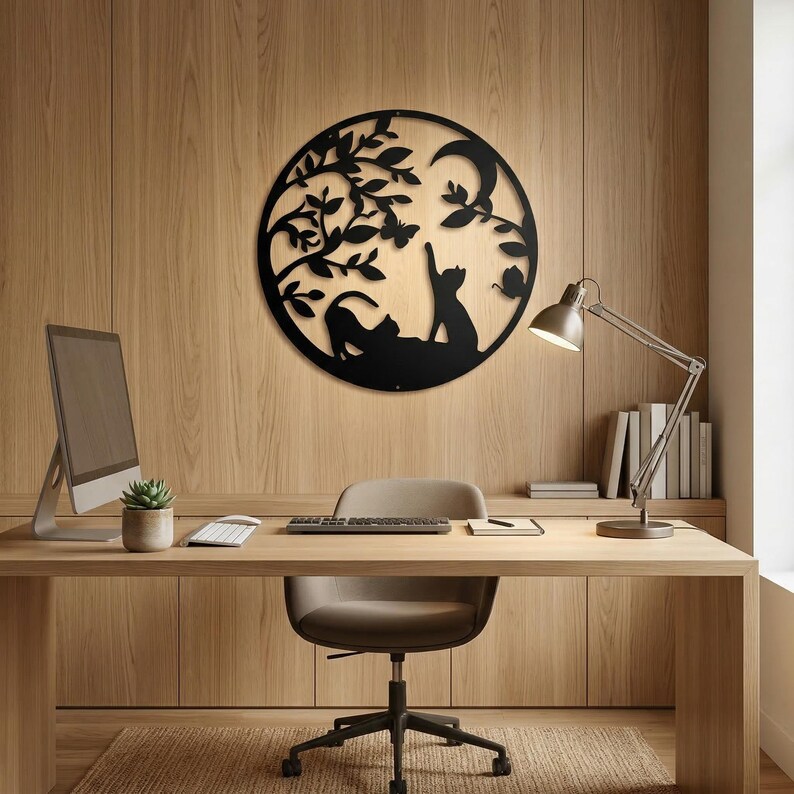 May include: Black metal wall art featuring a circular design with cat silhouettes under a tree, a crescent moon, and butterflies. The artwork is mounted on a wooden wall, creating a decorative piece for home or office decor.