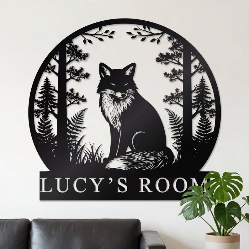 May include: Black metal wall art featuring a fox in a forest scene. The fox is centered within a circular frame with trees and foliage. The text "LUCY'S ROOM" is displayed at the bottom of the frame. The art is mounted on a white wall.