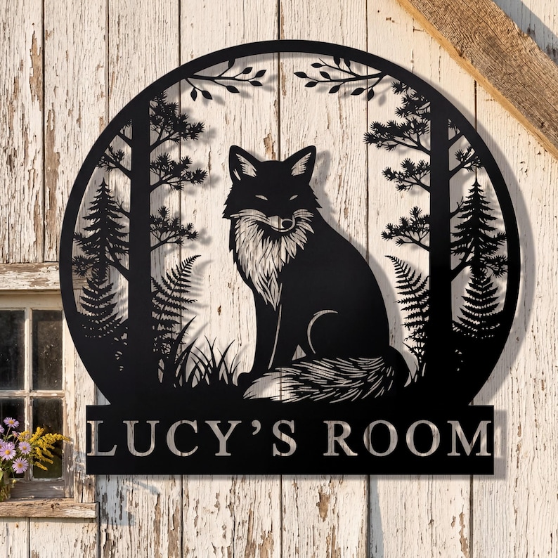 May include: Black metal wall art featuring a fox in a forest scene, framed by a circular design. The fox has a white chest and is surrounded by trees, ferns, and grass. The text "LUCY'S ROOM" is displayed below the circular design.