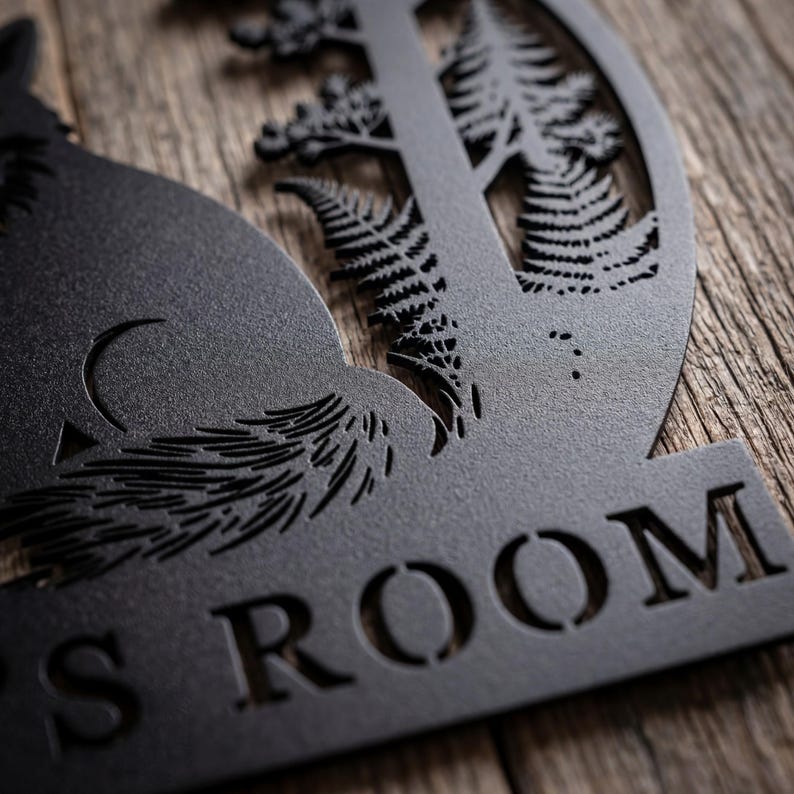 May include: Black metal wall art featuring a silhouette of a fox, trees, and ferns. The word "ROOM" is cut out at the bottom. The artwork is mounted on a wooden surface, creating a rustic aesthetic.