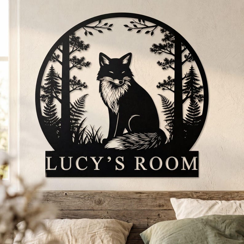 May include: Black metal wall art featuring a fox in a forest scene. The fox is centered within a circular frame with trees and foliage. The text "LUCY'S ROOM" is displayed below the fox. The art is mounted on a wooden wall.