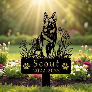 Könnte beinhalten: Ein schwarzer Metall-Gartenstecker mit der Silhouette eines Deutschen Schäferhundes, umgeben von Blumen. Der rechteckige Sockel zeigt den Namen Scout in einer Serifenschrift über den Jahren 2022-2025, flankiert von zwei Pfotenabdruck-Symbolen.