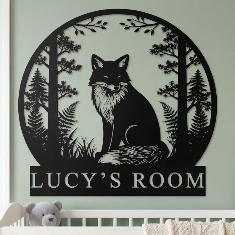 May include: Black metal wall art featuring a fox in a forest scene. The fox is centered within a circular frame with trees and foliage. The text "LUCY'S ROOM" is displayed below the frame. The artwork is mounted on a light green wall.