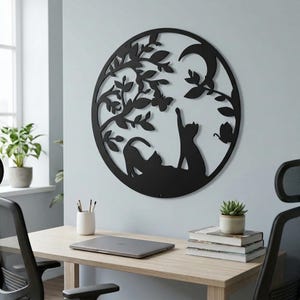 May include: Black metal wall art featuring a circular design with two cats, a tree, a crescent moon, and butterflies. The cats are in silhouette, one reaching up. The art is mounted on a light blue wall.