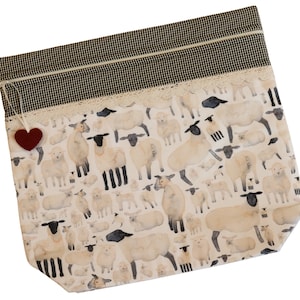 May include: A white zippered pouch with a black and white gingham trim and a white lace trim. The pouch is decorated with a pattern of watercolor sheep. A small red felt heart is attached to the zipper pull.