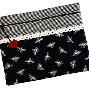 May include: Black zippered pouch with a white lace trim and a black and white gingham pattern on the top. The pouch has a red felt heart attached to the zipper pull and a black and white bee pattern on the bottom.