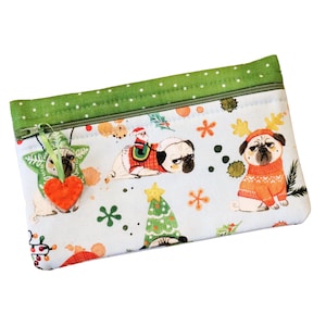 May include: A green and white zippered pouch with a Christmas theme. The pouch features a repeating pattern of pugs wearing festive attire, including Santa hats, reindeer antlers, and Christmas sweaters. The pouch also has a small red heart charm attached to it.
