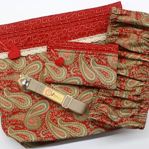 May include: Two red and gold paisley patterned zippered pouches with white lace trim and red pom-poms. The larger pouch has a tan strap with a silver clip.