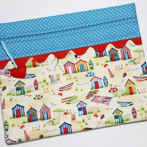 May include: A blue and white polka dot zippered pouch with a red and white scalloped trim. The pouch is decorated with a beach scene featuring colorful beach huts, surfboards, and umbrellas.