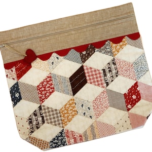 Könnte beinhalten: Eine handgefertigte Patchwork-Reißverschlusstasche mit einem geometrischen Würfeldesign. Die Tasche hat eine Vielzahl von gemusterten Stoffen in Rot, Weiß, Braun und Blau. Ein roter Herzanhänger hängt am Reißverschluss. Die Oberseite ist aus beigem Stoff.