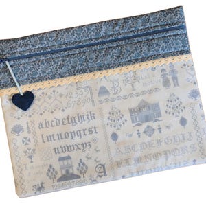 May include: A white fabric zippered pouch with a blue floral pattern on the outside. The pouch has a black heart sewn on the front and a white lace trim. The fabric has a cross-stitch design with numbers, letters, and a house.