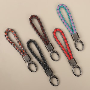 Puede incluir: Cinco llaveros trenzados en varios colores: naranja y gris, marrón y gris, negro, rojo y gris, y turquesa y morado. Cada llavero tiene un cierre de metal y una base de metal a juego.