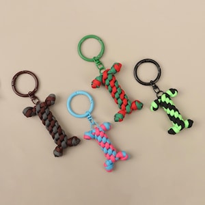 Puede incluir: Una colección de llaveros hechos a mano en varios colores. Los llaveros tienen forma de la letra "I" y están hechos de cordón trenzado. Los colores incluyen marrón, rojo y verde, negro y verde, y azul y rosa. Cada llavero tiene un anillo de metal.