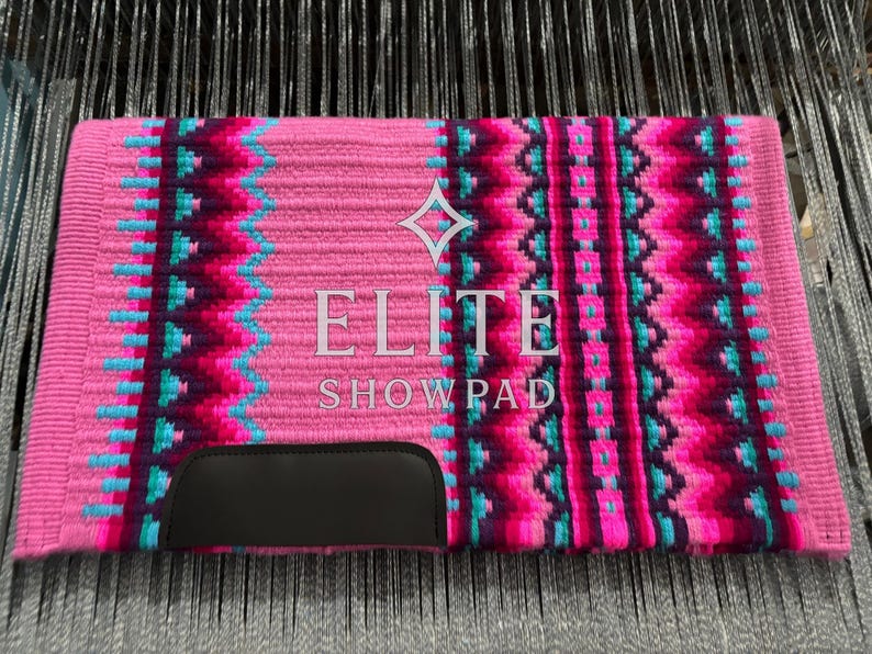 May include: A pink horse show pad with a geometric pattern in teal, magenta, and dark purple. The pad features the text "ELITE SHOWPAD" in white and a black leather reinforcement at the bottom.