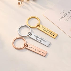Può includere: Tre portachiavi con ciondoli rettangolari e anelli tondi. Uno è dorato con inciso "Always In Our Herats We Love You Mom". Un altro è argentato con "bestfriend forever Est.2024". Il terzo è oro rosa con "Drive safe my love".