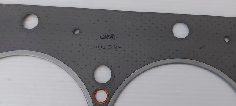 Puede incluir: Una junta gris con m&uacute;ltiples agujeros circulares y un borde de metal plateado. Los textos "SECTOR" y "specs50" est&aacute;n impresos en la junta. Un anillo de color cobre es visible en la parte inferior.