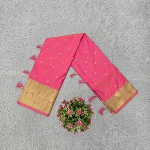 K&ouml;nnte beinhalten: Ein leuchtend rosa Sari mit goldenen Punkten und einem goldenen Rand. Der Sari ist an den Enden mit passenden rosa Quasten verziert. Eine kleine Blumengesteck befindet sich in der N&auml;he des Saris.