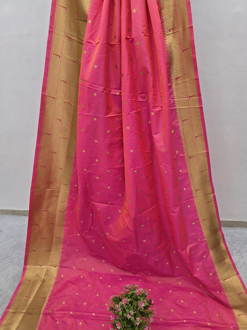 K&ouml;nnte beinhalten: Ein leuchtend pinkfarbenes Textil mit einem goldenen Rand und kleinen goldenen Tupfen. Der Stoff ist drapiert und zeigt seine Textur und seinen Glanz. Der goldene Rand verleiht dem Design einen Hauch von Eleganz.