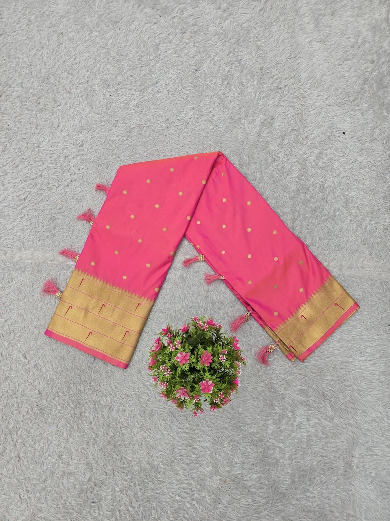 K&ouml;nnte beinhalten: Ein leuchtend rosa Sari mit goldenen Punkten und einem goldenen Rand. Der Sari ist an den Enden mit passenden rosa Quasten verziert. Eine kleine Blumengesteck befindet sich in der N&auml;he des Saris.